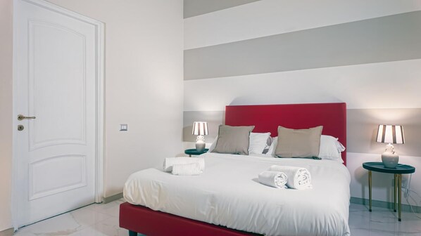 A neatly made bed with white linens, a red headboard, and two bedside tables with lamps. - Popolo Guest Rooms (Roma)