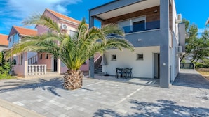 A modern two-story house with a balcony, a palm tree in the front yard, and a paved driveway. - 1 bedroom cozy apartment in Vir (Vir)