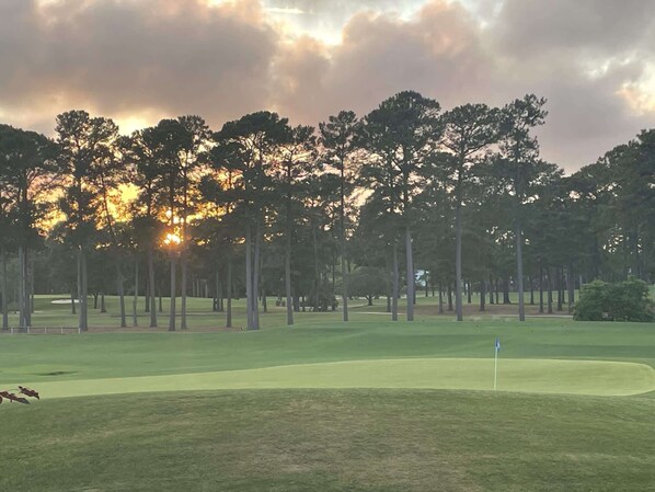 A golf course with a flagstick, trees, and a sunset. - World Tour Unit 206 - Overlooking the 18th Green (Myrtle Beach)