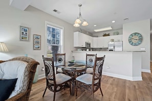 Cozy living space with a round dining table and wicker chairs, kitchenette with refrigerator and microwave.