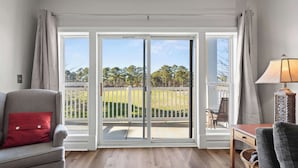 Una habitación con puerta corrediza de vidrio que da a un balcón con vistas a un área verde y árboles.