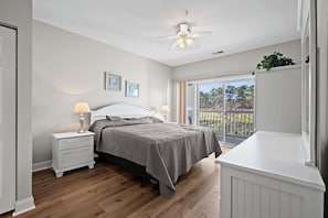 Relax in this serene bedroom with a single bed, bedside tables, and a ceiling fan, offering a peaceful view from the balcony.