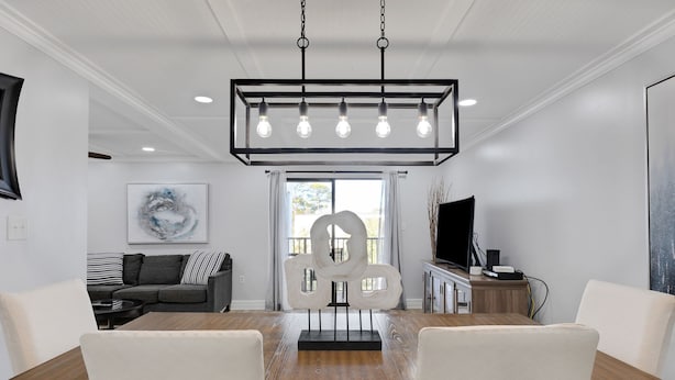 A dining area with a wooden table, white chairs, a modern chandelier, and a contemporary art piece.
