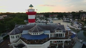 A waterfront property with a lighthouse, multiple boats docked, and a building with outdoor seating.