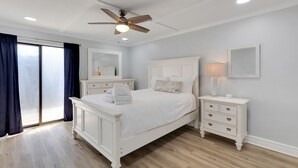 A bedroom with a white bed, a nightstand, a mirror, and a ceiling fan.
