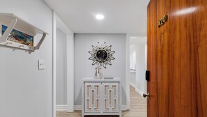 A hallway with a wooden door labeled "A20," a white console table with a decorative mirror, and a small shelf with books.
