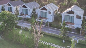 A row of modern, white cottages with sloped roofs, surrounded by lush greenery and a mountain backdrop. - The Estretto Resort (Wiang Chiang Rung)