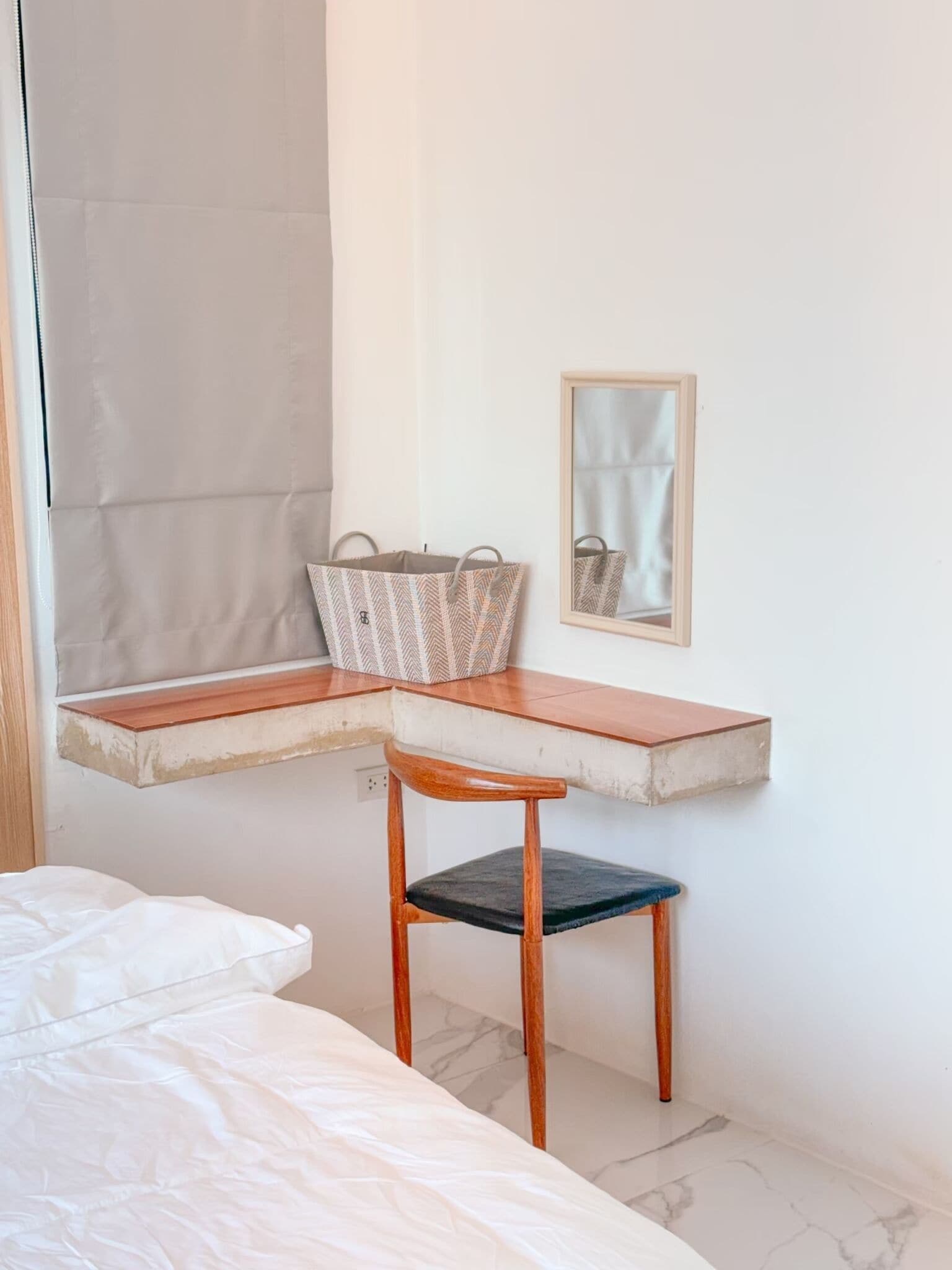 A small, compact room with a bed, a desk with a chair, a mirror, and a wall-mounted shelf.