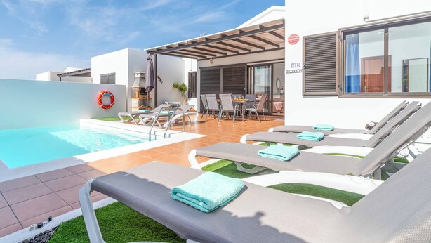 A modern outdoor pool area with lounge chairs and a covered patio. - Villa Elma (Yaiza)