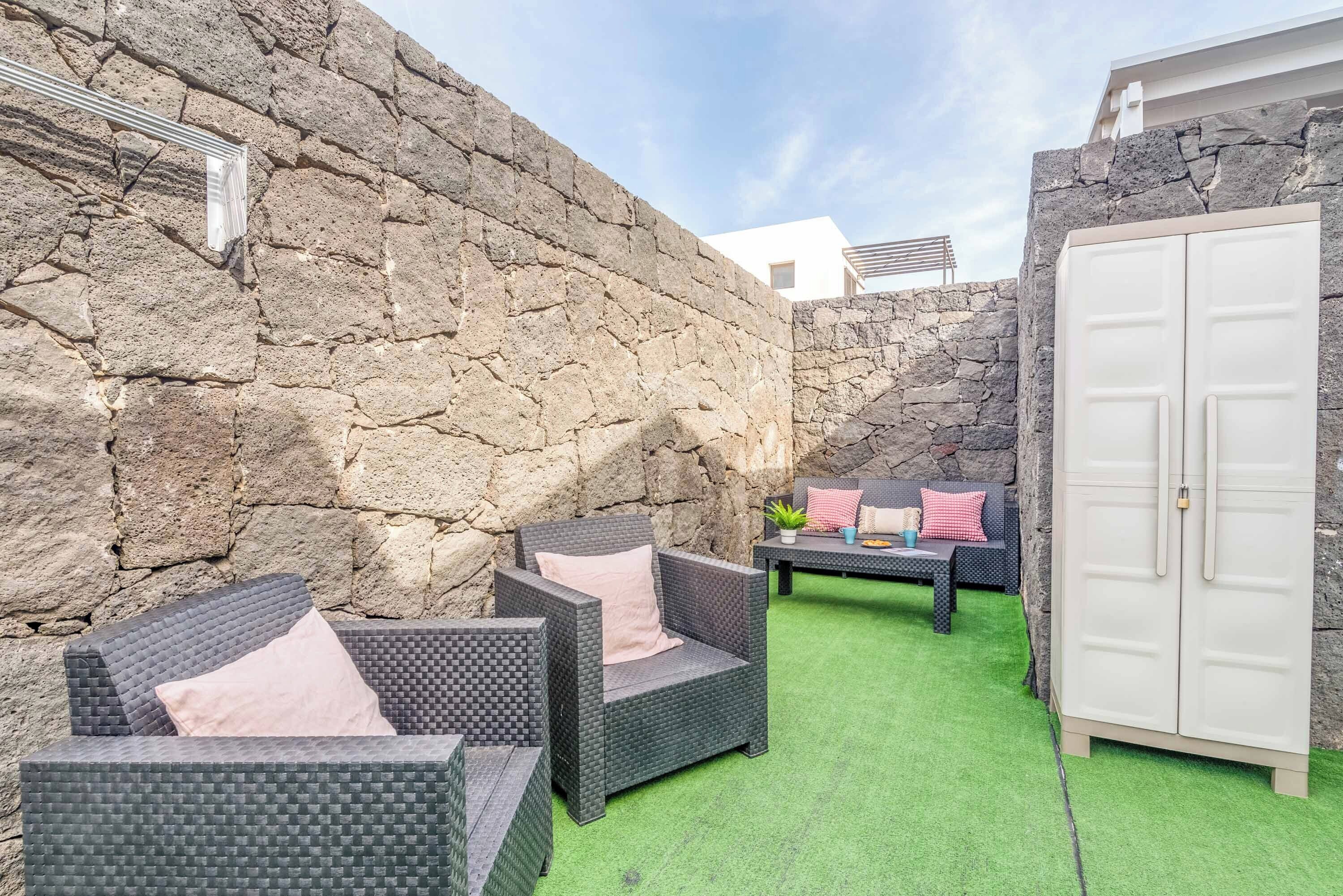 A patio area with wicker furniture, a stone wall, and a white wardrobe.