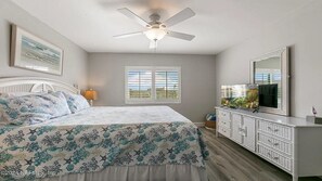 A bedroom with a bed, a ceiling fan, a dresser, a TV, and a window with blinds.