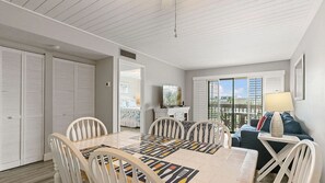 A dining area with a table and chairs, a television, and a balcony with a view.