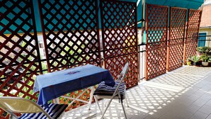Eine überdachte Terrasse mit Tisch und Stühlen, einem Gitterzaun und Topfpflanzen.