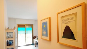 Ein Flur mit gerahmten Kunstwerken an den Wänden, einer weißen Vitrine mit Glastüren und Blick in einen Raum mit einer Schiebetür.