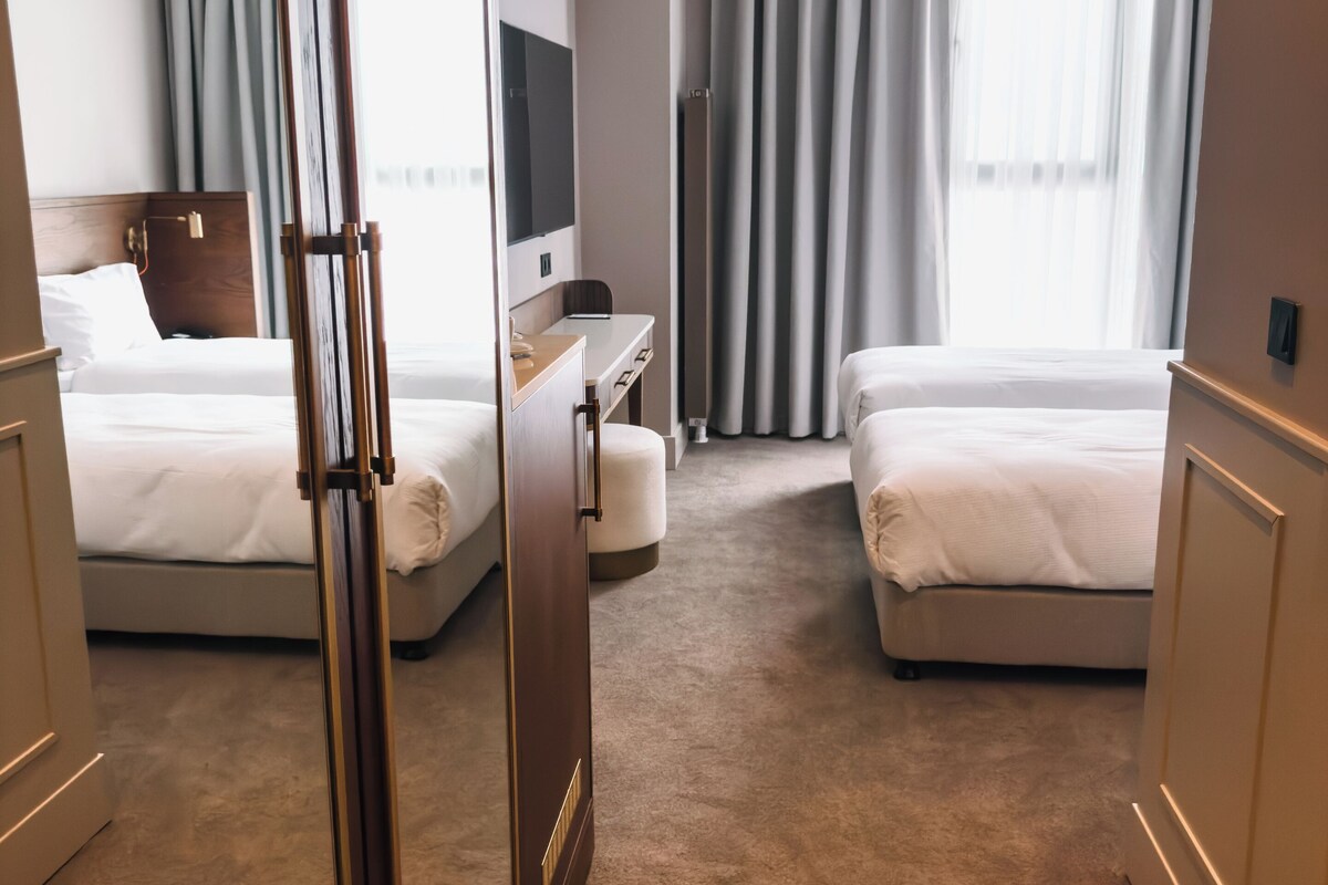 Une chambre d’hôtel avec deux lits, un bureau, une télévision et une grande fenêtre avec des rideaux.