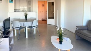 A modern living room with a dining area, a grey sofa, a flat-screen TV, and a small table with a plant.
