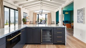 A modern kitchen with dark cabinetry, a marble countertop, and a central island. - Vintner's Village | California-Chic Wine Estate (Temecula)