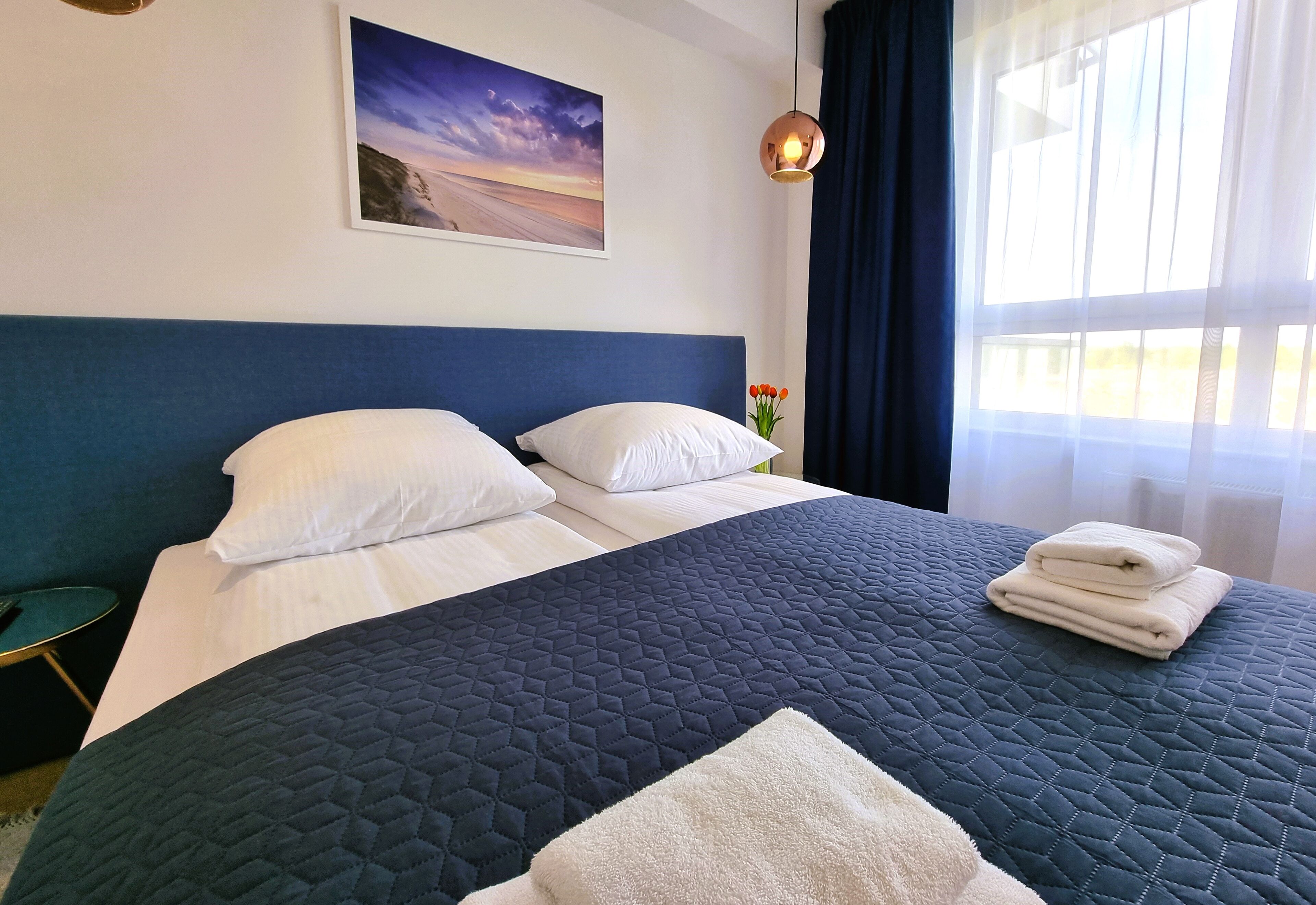 A neatly made bed with a blue quilt, white pillows, and folded towels on a dark blue headboard.