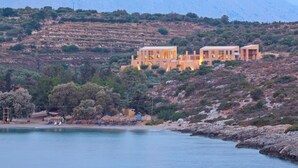 A coastal property with two main buildings, a beach with umbrellas, and a rocky hillside. - Chania Olea Villa - Breathtaking Summer Getaway (Chania)