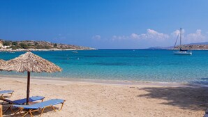 A beach with clear blue water, a boat, and lounge chairs. - Chania Olea Villa - Breathtaking Summer Getaway (Chania)