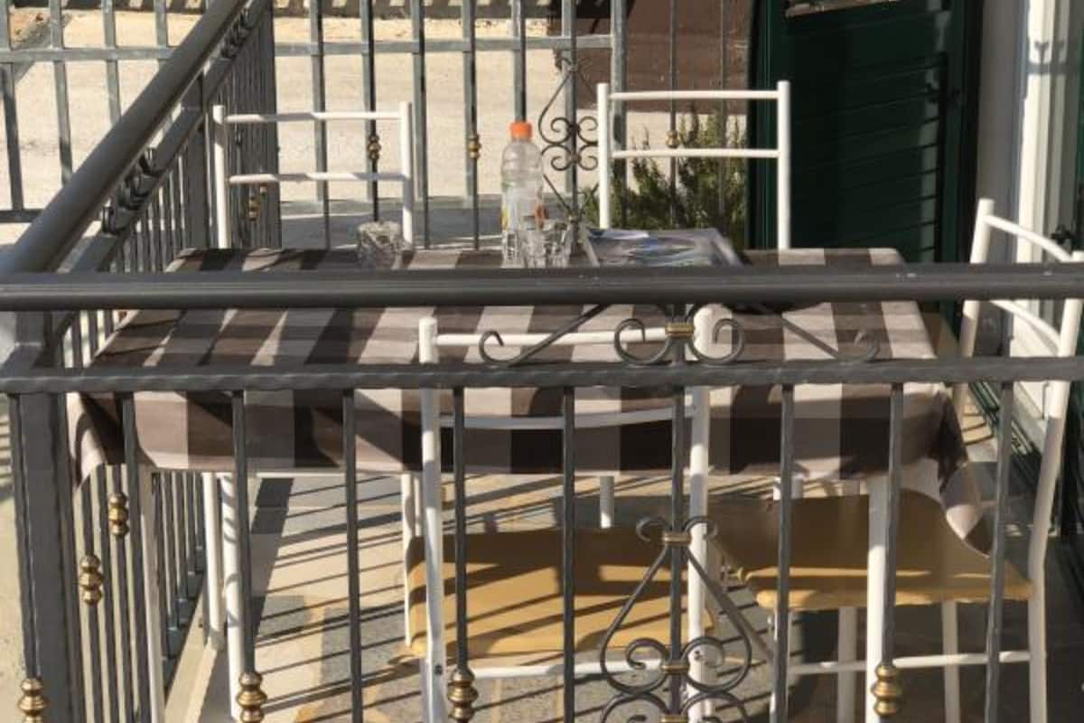 Un balcon doté d’un sol à carreaux, d’une rambarde en métal et d’une table sur laquelle se trouvent une bouteille et des verres.