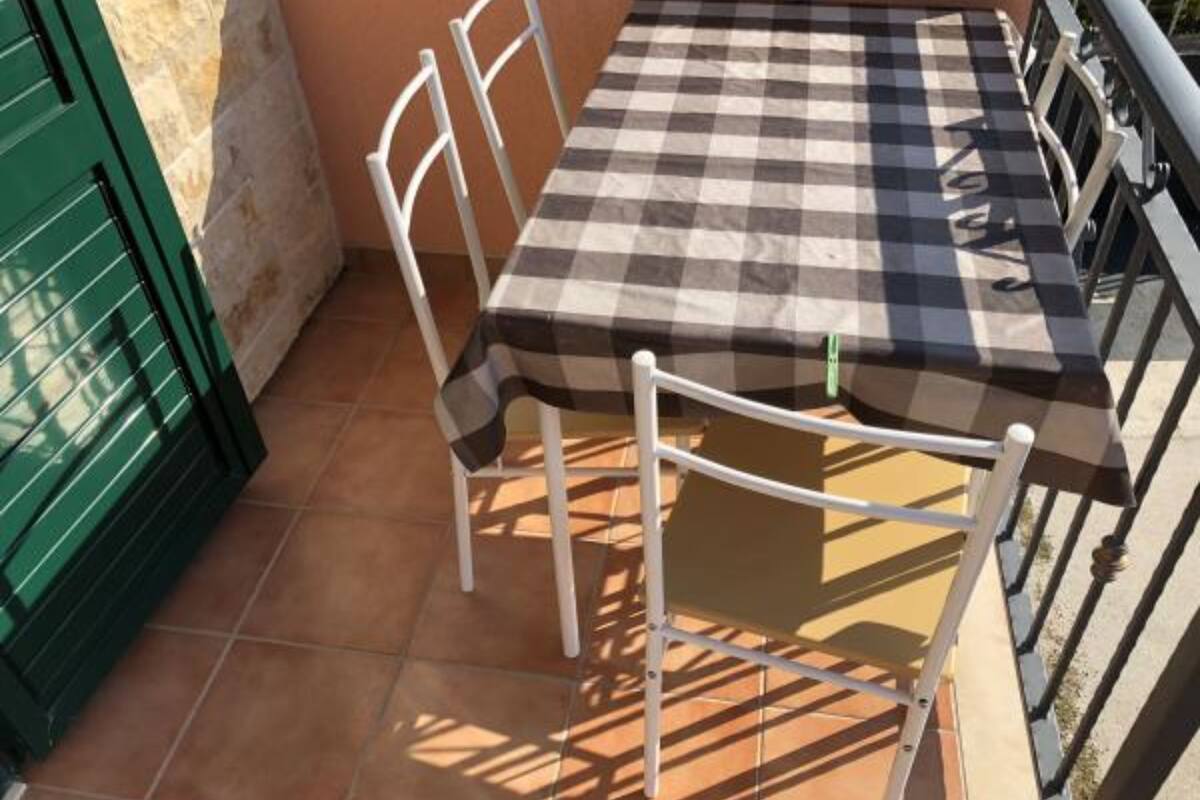 Une terrasse avec une table à carreaux et des chaises blanches, entourée d’une rambarde en métal.