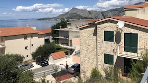 A coastal residential area with stone buildings, a view of the sea, and mountains in the background. - Apartmani Villa Borzic (Omis)