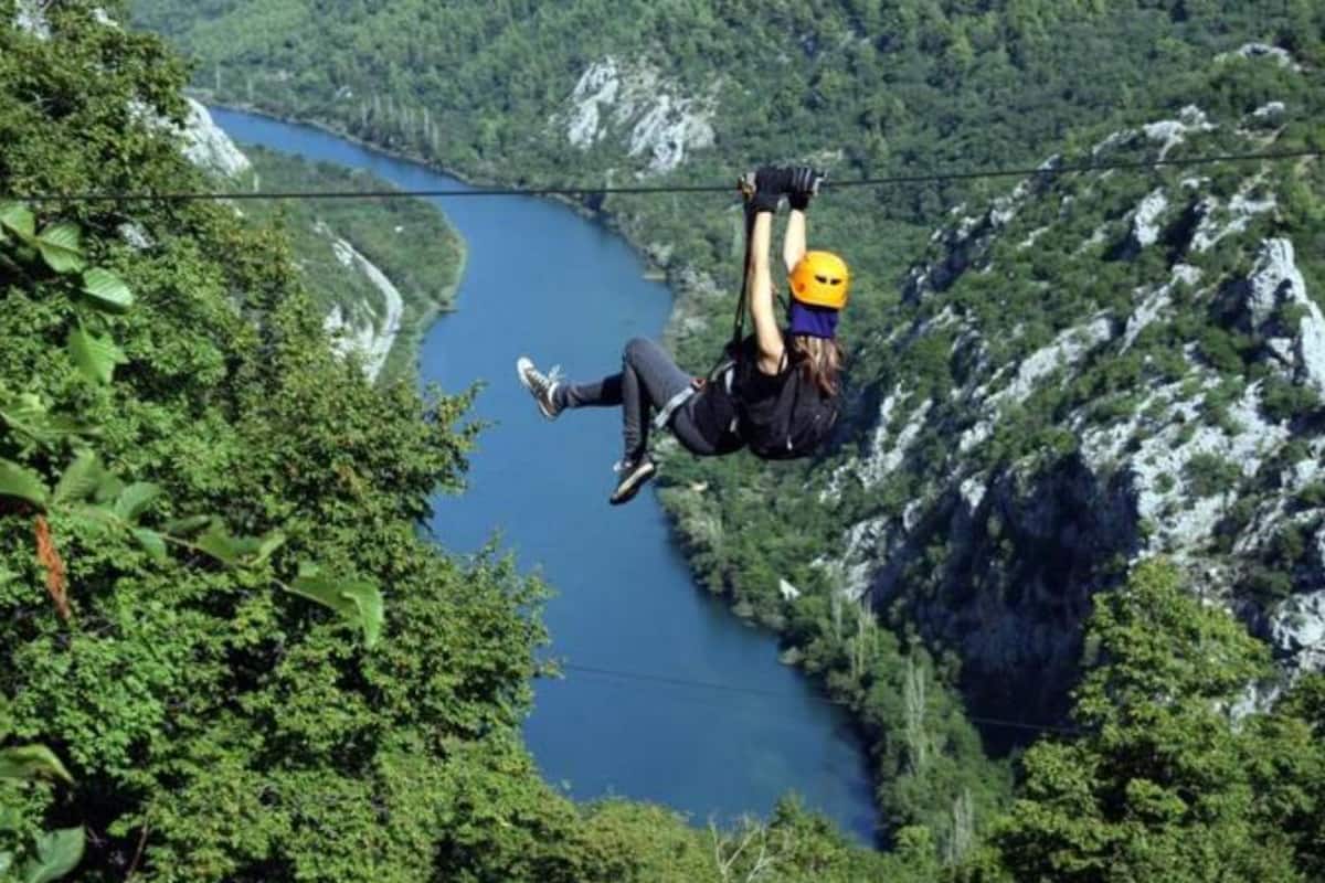 Une personne pratiquant le saut à l’élastique, avec une rivière et des montagnes en arrière-plan.