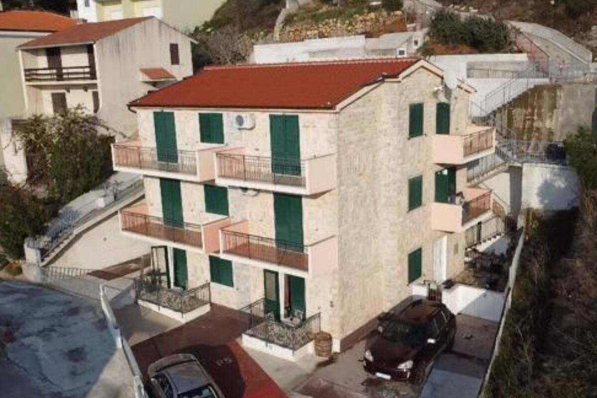 Un immeuble à plusieurs étages, doté de balcons et d’un toit rouge, avec une voiture garée devant.