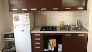 A compact kitchen with brown cabinets, a white refrigerator, a microwave, a stove, and a sink. - Apartmani Villa Borzic (Omis)