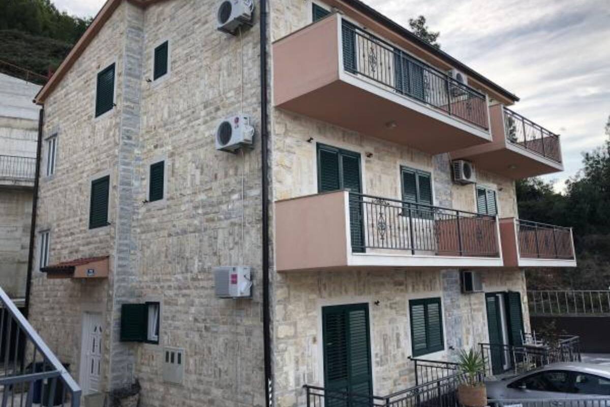Un immeuble à deux étages avec des murs en pierre, de nombreux balcons et des unités de climatisation.