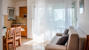 A modern living room with a sofa and chairs, a kitchen area with wooden cabinets, and a sliding glass door leading to a balcony. - Apartmani Martinović (Gradac)