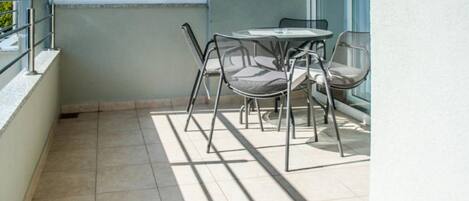 Ein Balkon mit Tisch und Stühlen, ein Fenster mit Milchglas und ein gefliester Boden.