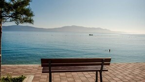 A bench on a paved area overlooking a calm body of water with distant mountains. - Apartmani Martinović (Gradac)