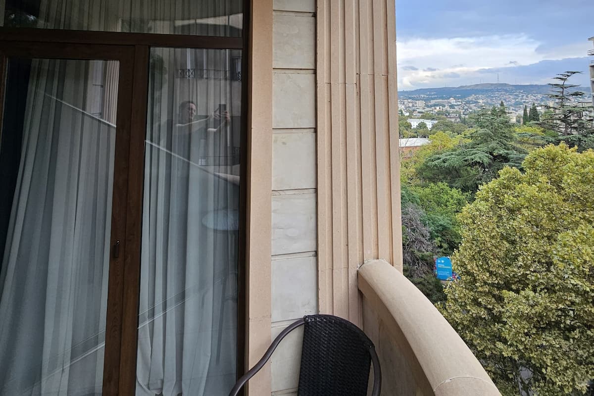 A balcony with a wicker chair, a window with curtains, and a view of a cityscape.