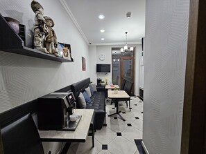 A modern interior with a black leather sofa, a coffee machine, and a dining area with a table and chairs. - Hotel Giorgi (Tbilisi)