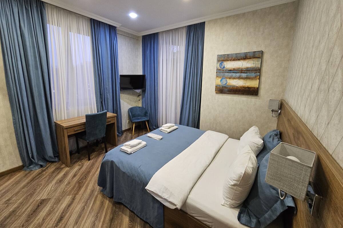 A hotel room with a bed, a desk, a chair, and a TV.