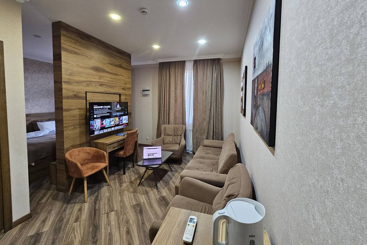 A modern hotel room with a wooden accent wall, a flat-screen TV, a sofa, a coffee table, and a bed with a headboard.