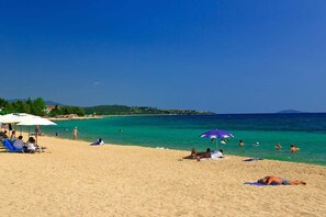 A beach with people sunbathing and swimming, umbrellas, and a clear blue sky.