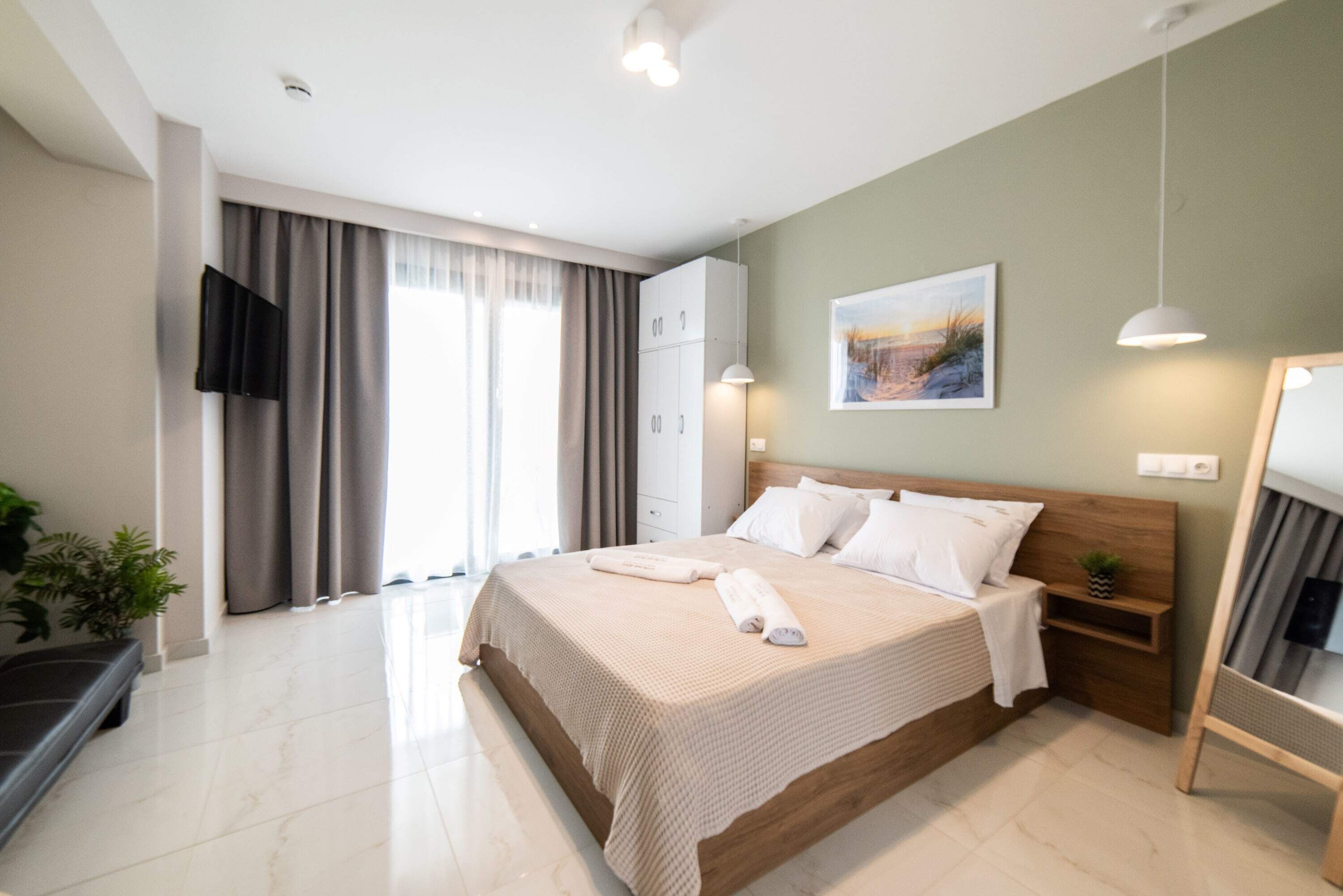 A modern bedroom with a large bed, a flat-screen TV, a wardrobe, and a window with curtains.