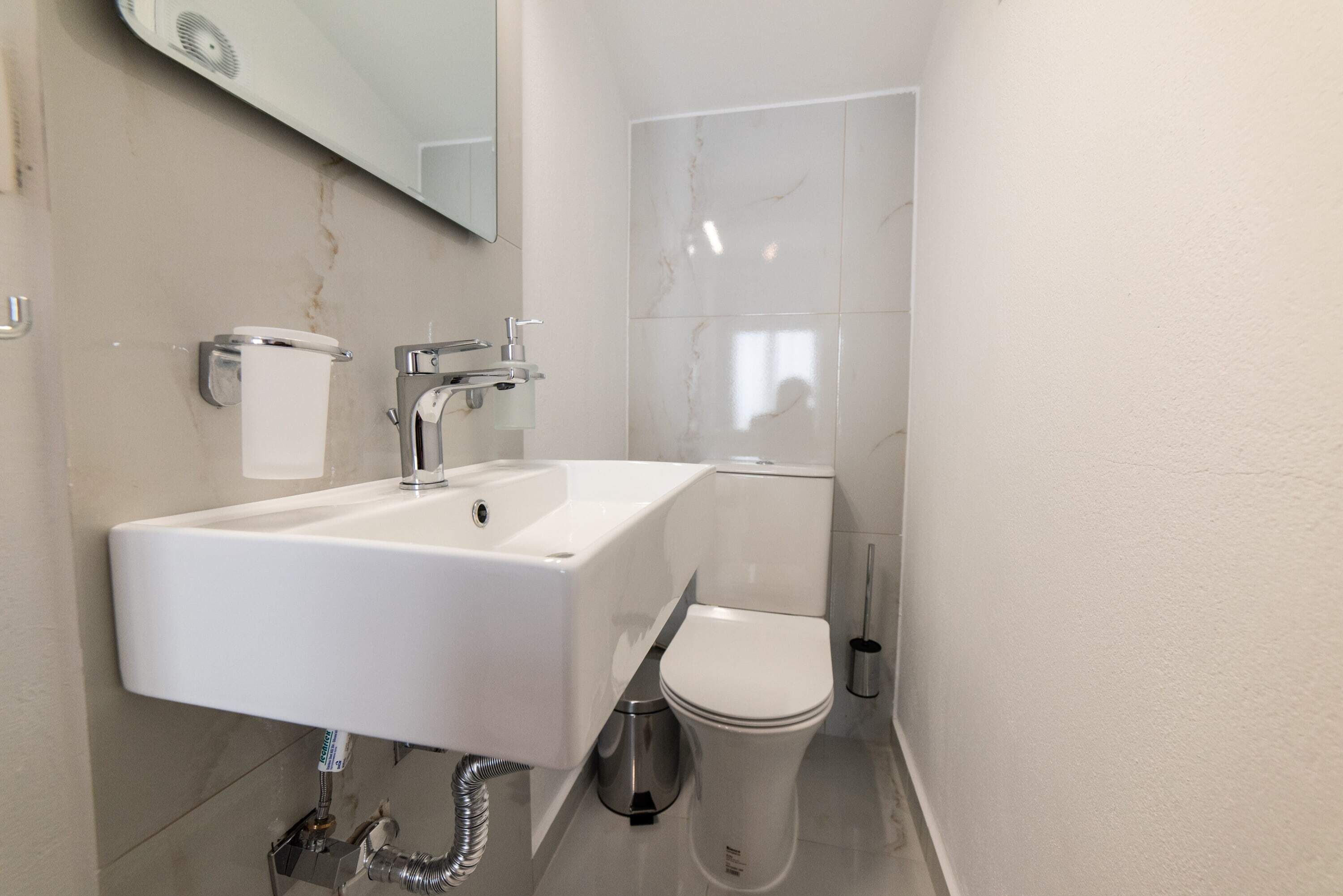 Un baño moderno con lavamanos, inodoro y espejo blancos.