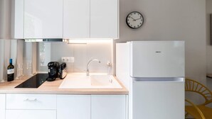 Een moderne keuken met witte kasten, een zwart aanrecht, een witte spoelbak, een koffiezetapparaat, een wijnfles en een klok aan de muur.