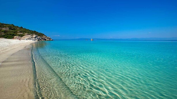 Een helder strand met turquoise water, een zandstrand en een klein bootje in de verte.