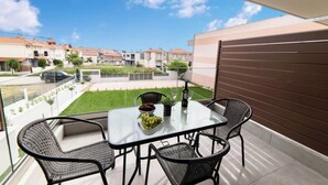 Een balkon met een glazen tafel, vier rieten stoelen, een fruitschaal, een fles en een glas.