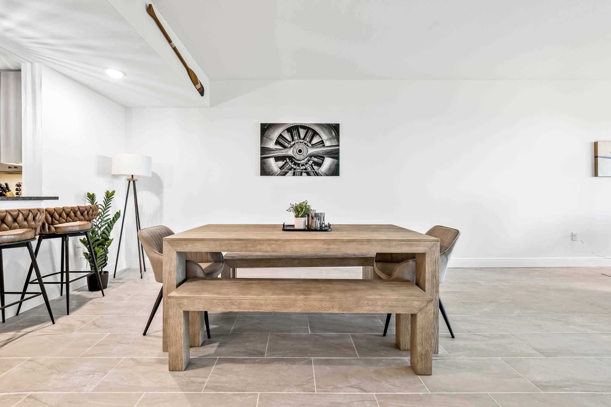 A dining area with a wooden table, benches, and a wall-mounted artwork.