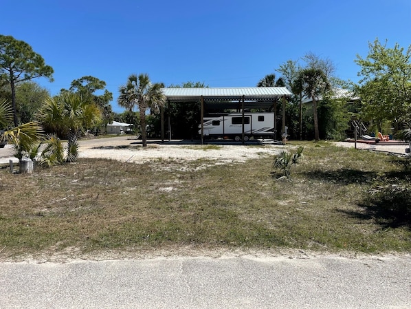 A covered RV park with a white RV, palm trees, and a clear blue sky.