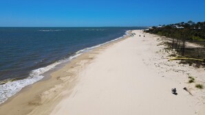 A wide sandy beach with gentle waves, a clear blue sky, and sparse vegetation. - RV LOT Pole barn is fully covered and concreted Indian Pass (Port Saint Joe)