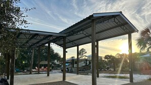 A covered outdoor area with a gravel floor, a metal roof structure, and a parked RV. - RV LOT Pole barn is fully covered and concreted Indian Pass (Port Saint Joe)