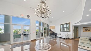 A spacious lobby with a grand chandelier, a piano, a white sofa, and a glass display case. - RIVER FLY IN: The Cocoa, Launchpad Lookout View (Merritt Island)