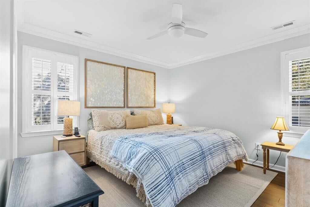 A bedroom with a bed, two bedside lamps, a ceiling fan, and a window with blinds.